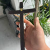 A hand holds a dark wood crucifix with a gold-colored nail, against a blurred green plant background.