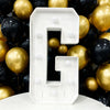 A large white marquee light-up letter G is displayed against a backdrop of gold and black balloons.