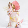 A four-tiered cake decorated with pink and gold flowers, including a palm leaf topper.