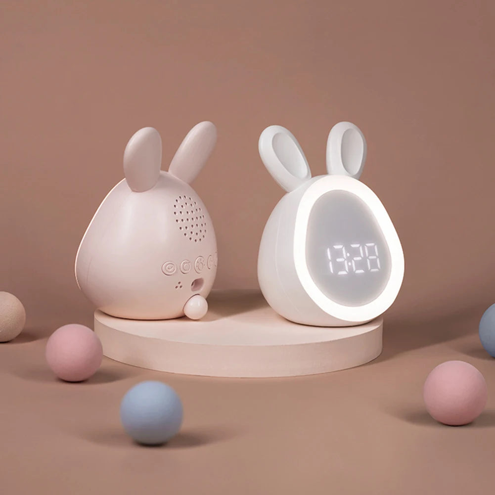 A pink mini LED cartoon alarm clock night light with rabbit ears sitting on a light wooden stand.
