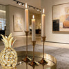A set of three ornate vintage metal candle holders with tall white candles displayed on a reflective surface.