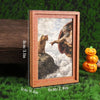 A framed art print featuring a cat looking out of a bowl against a cloudy sky, displayed on green grass.