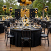 A round table set for an elegant event with black linens, gold accents, and dark floral centerpieces.
