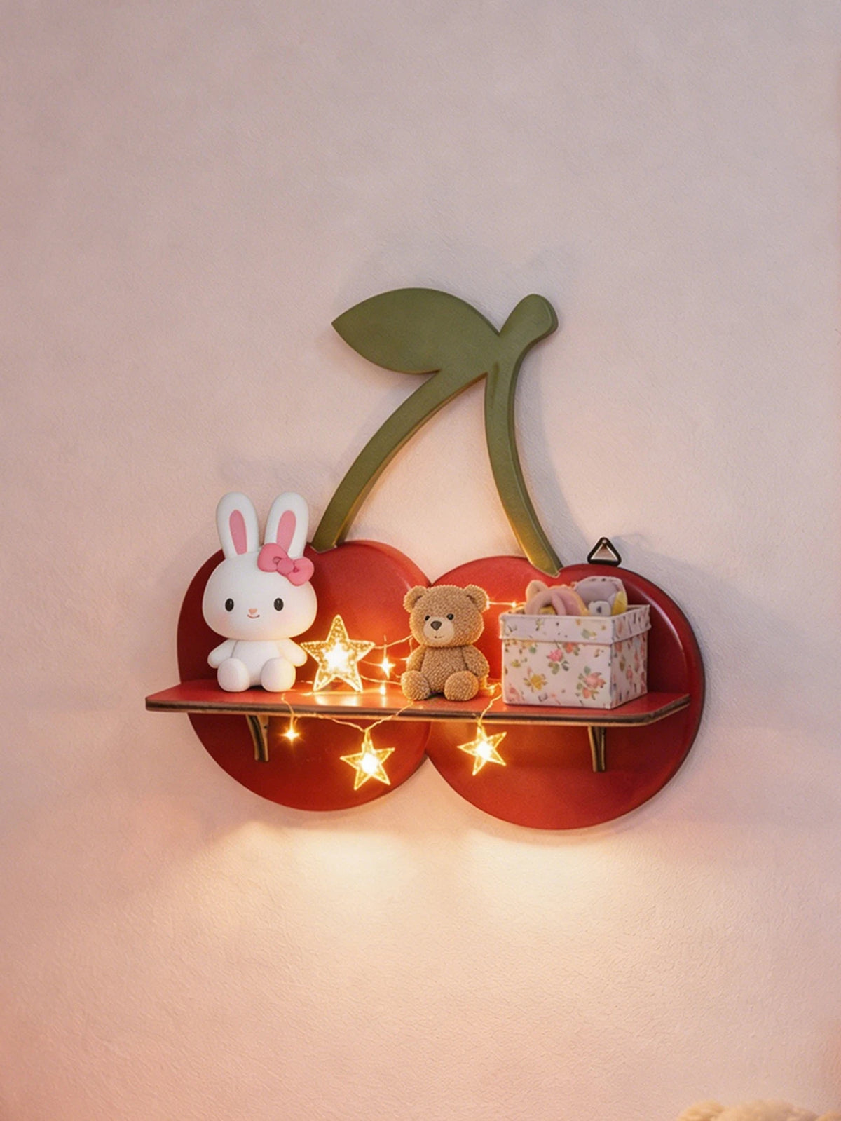 A wooden shelf shaped like a cherry with a green leaf, holding a white rabbit and a teddy bear.