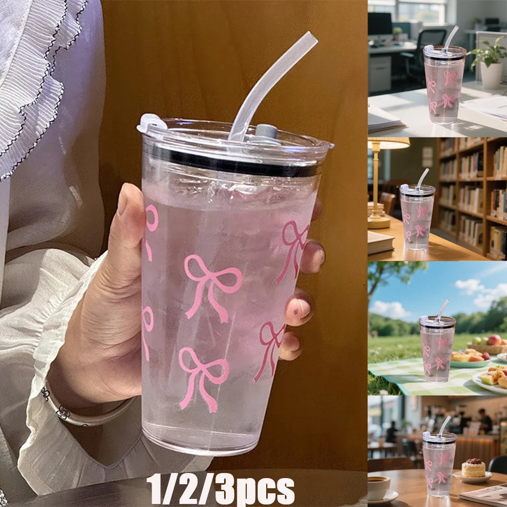 A hand holds a clear pink plastic cup with a lid and straw, featuring a decorative pink bow design.