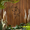 Black silhouette of a cat and woman forms metal wall art against a warm wooden slat background with greenery.