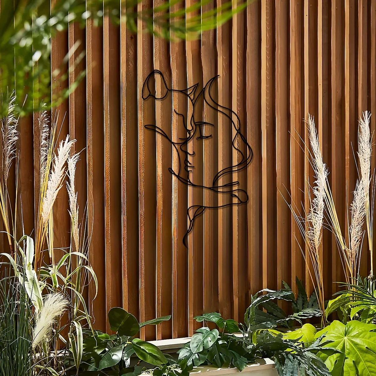 Black silhouette of a cat and woman forms metal wall art against a warm wooden slat background with greenery.