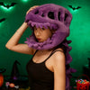 A woman wearing a purple dinosaur skeleton costume headpiece against a green background.