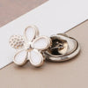 Silver floral brooch buttons with pearl accents resting on a light beige surface.