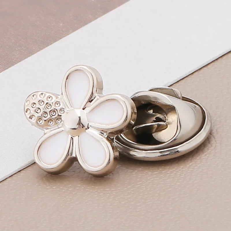 Silver floral brooch buttons with pearl accents resting on a light beige surface.