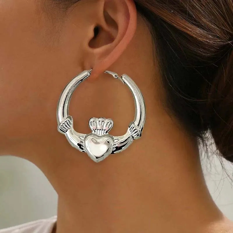 Silver hoop earrings with a heart charm worn on the ear of a woman.