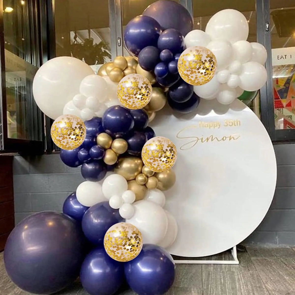 A balloon garland arch featuring navy blue, silver, gold, and white balloons for a birthday celebration.
