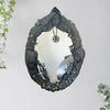 A dark, leafy wreath mirror frame featuring a face and a hanging pentagram amulet.