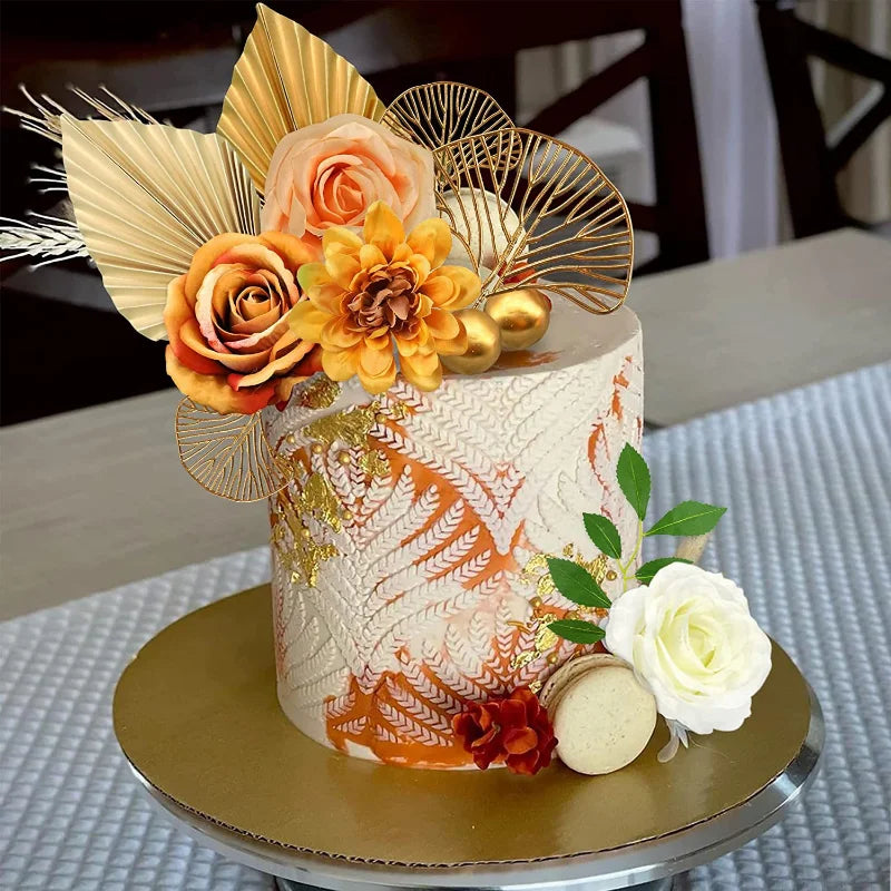 A tiered cake decorated with orange and gold floral elements and palm leaf toppers.