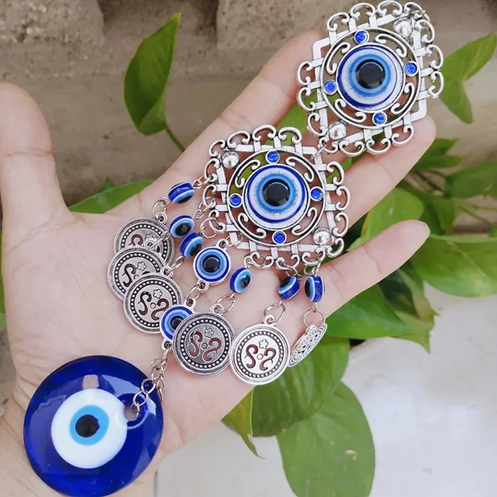 Silver and blue Turkish evil eye hamsa hand amulet jewelry displayed in a person's hand against green foliage.