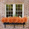An orange and white artificial daisy bouquet displayed in a black planter on a brick wall.