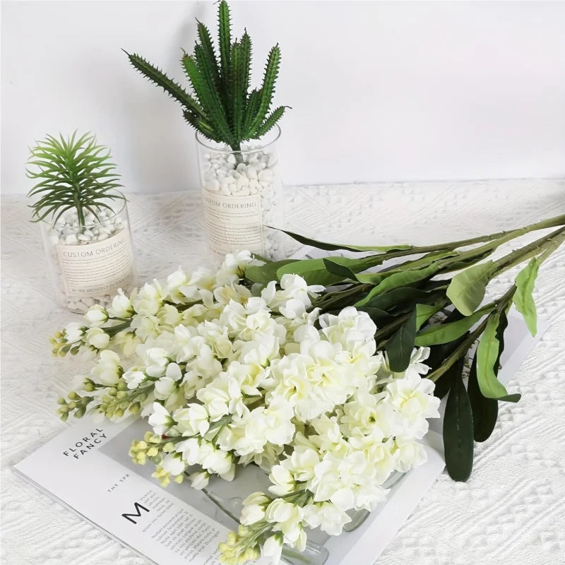A bouquet of artificial white delphinium flowers displayed on a white surface.