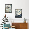 A set of two framed botanical prints displayed on a white wall above a wooden cabinet and chair.