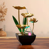 A golden tabletop fountain featuring green leaves and water spouts in a black bowl.