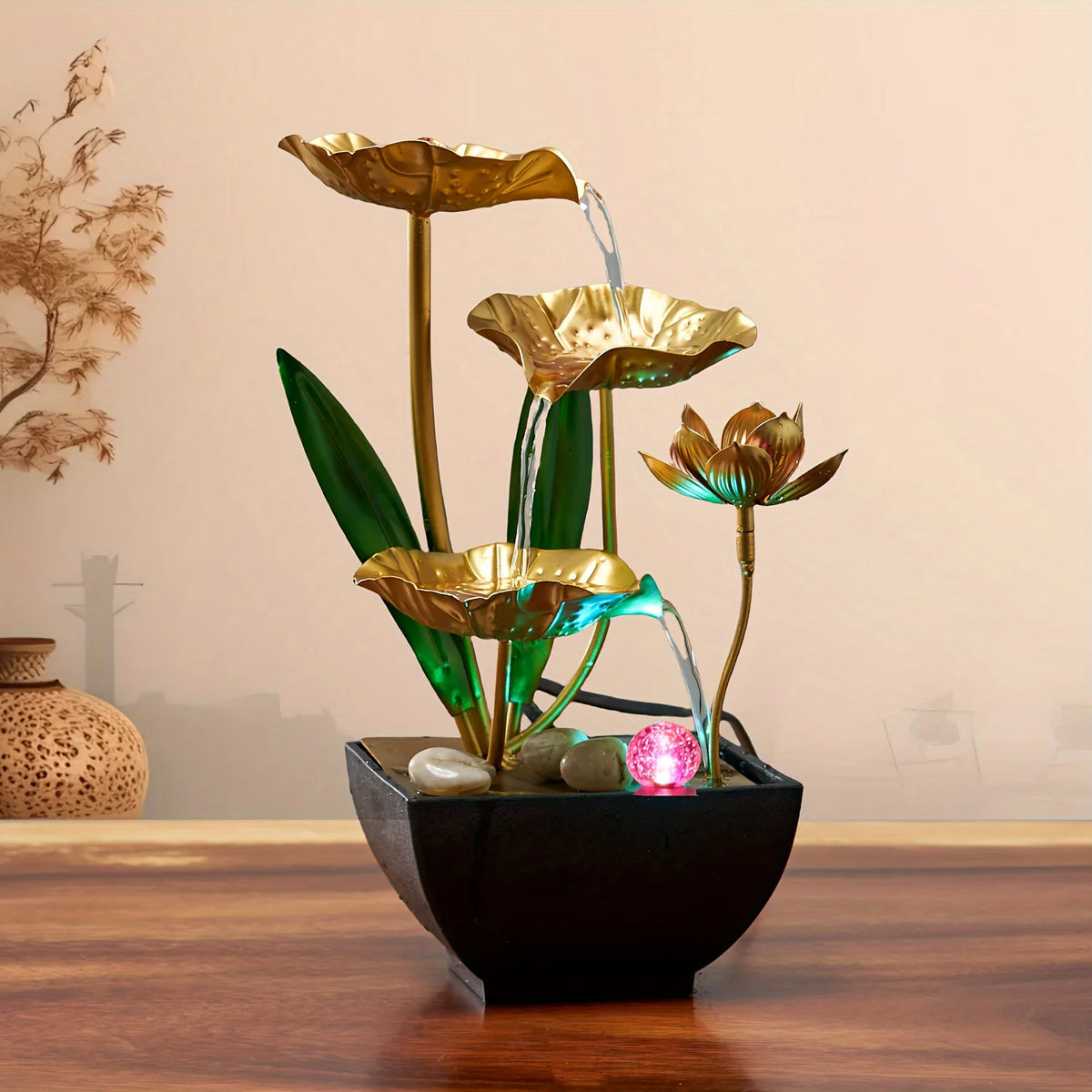 A golden tabletop fountain featuring green leaves and water spouts in a black bowl.