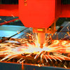 A close-up of a machine using a laser to cut or etch metal, creating bright sparks on a wooden surface.