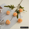 Artificial chrysanthemum pompon flowers in orange and green on a white background