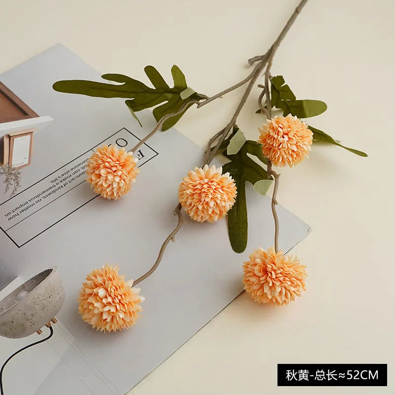 Artificial chrysanthemum pompon flowers in orange and green on a white background