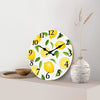 A round wall clock face decorated with yellow lemons and green leaves, set against a light background.