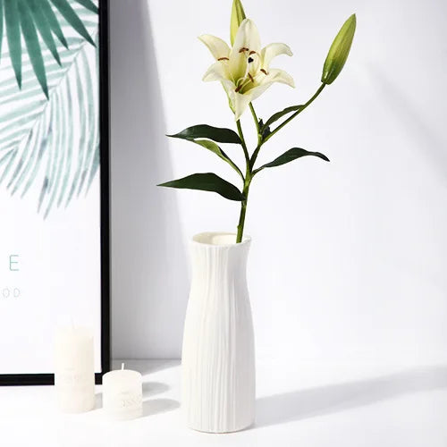A white ceramic vase holds a single white orchid stem against a bright background.