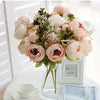 A bouquet of pink and cream peony artificial flowers with green foliage displayed in a glass vase.
