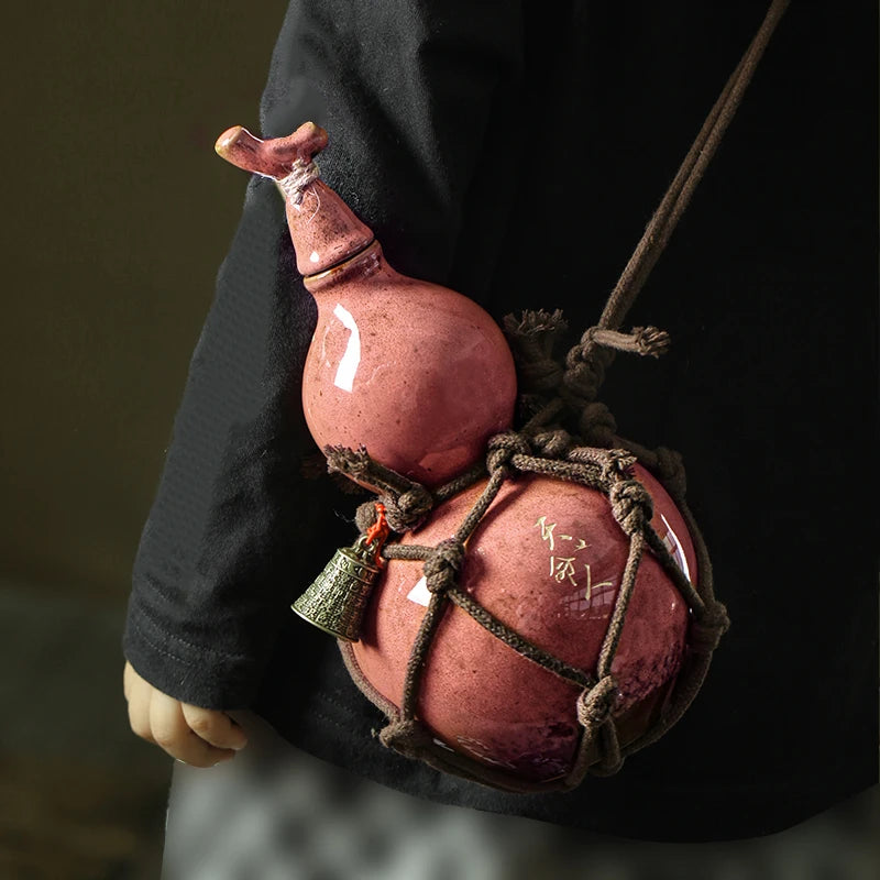 A traditional ceramic wine gourd with a narrow neck is suspended by twine, featuring an engraved mark.