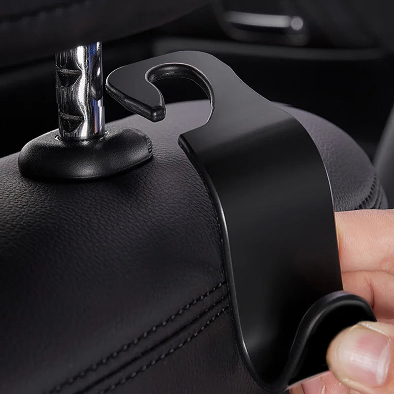 A close-up of black car headrest hooks designed for bag storage, showing the hook mechanism and leather upholstery.