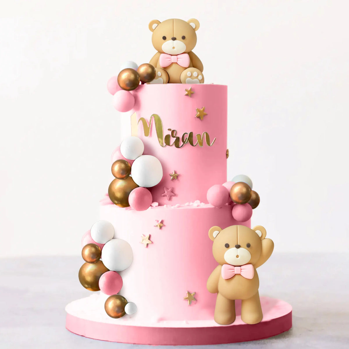 A pink tiered cake decorated with gold and white bear figures and spherical decorations.