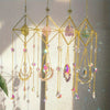 A collection of hanging crystal prisms and beads in various colors suspended from a gold wire frame.