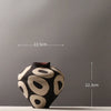 A black ceramic vase with geometric circle designs on a gray background.