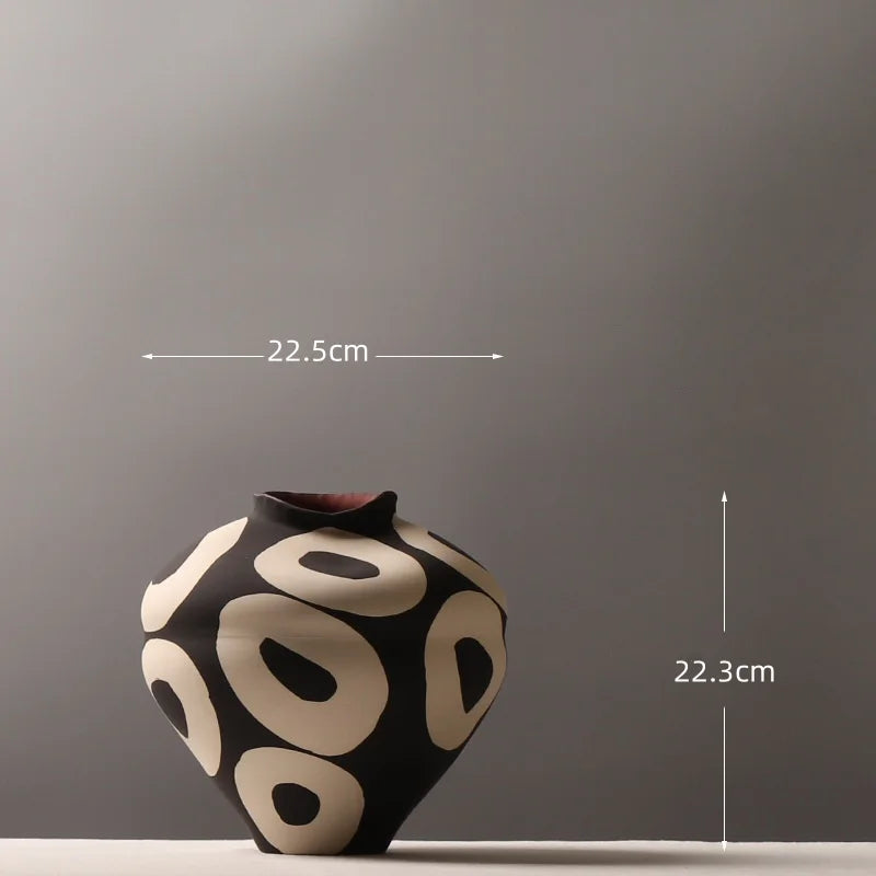 A black ceramic vase with geometric circle designs on a gray background.