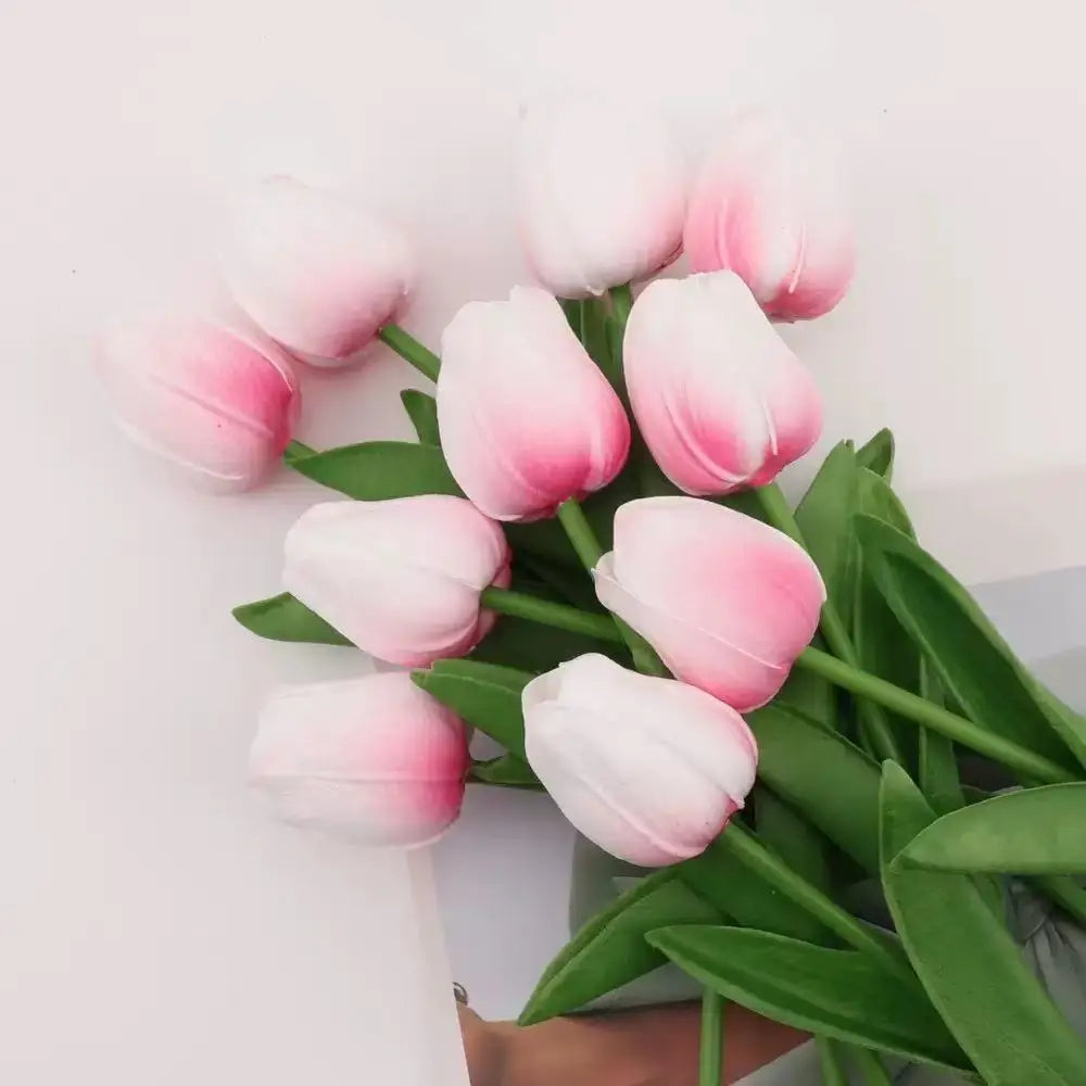 A bouquet of pink and white artificial tulips with green stems arranged on a white surface.