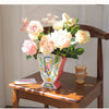 A floral arrangement of pink and cream roses in a vintage ceramic bird vase on a wooden table.