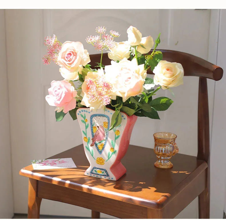 A floral arrangement of pink and cream roses in a vintage ceramic bird vase on a wooden table.