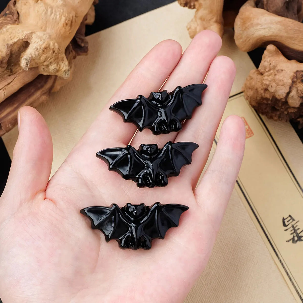 Three black hand-carved obsidian bat figurines displayed on a person's palm.