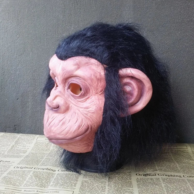A realistic latex monkey mask with pinkish skin and black fur, displayed against a gray background.