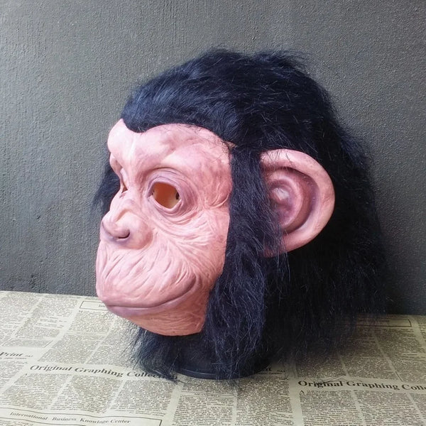 A realistic latex monkey mask with pinkish skin and black fur, displayed against a gray background.