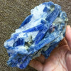 A hand holds a vibrant blue kyanite crystal stone with sharp facets and translucent edges.