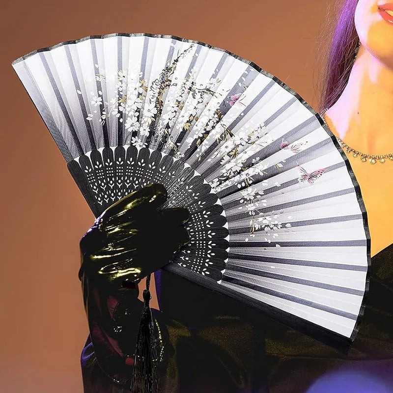 A close-up of a vintage silk bamboo folding hand fan with delicate floral designs, held by a person.