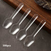 A set of 500 clear plastic disposable spoons arranged on a dark wooden surface.