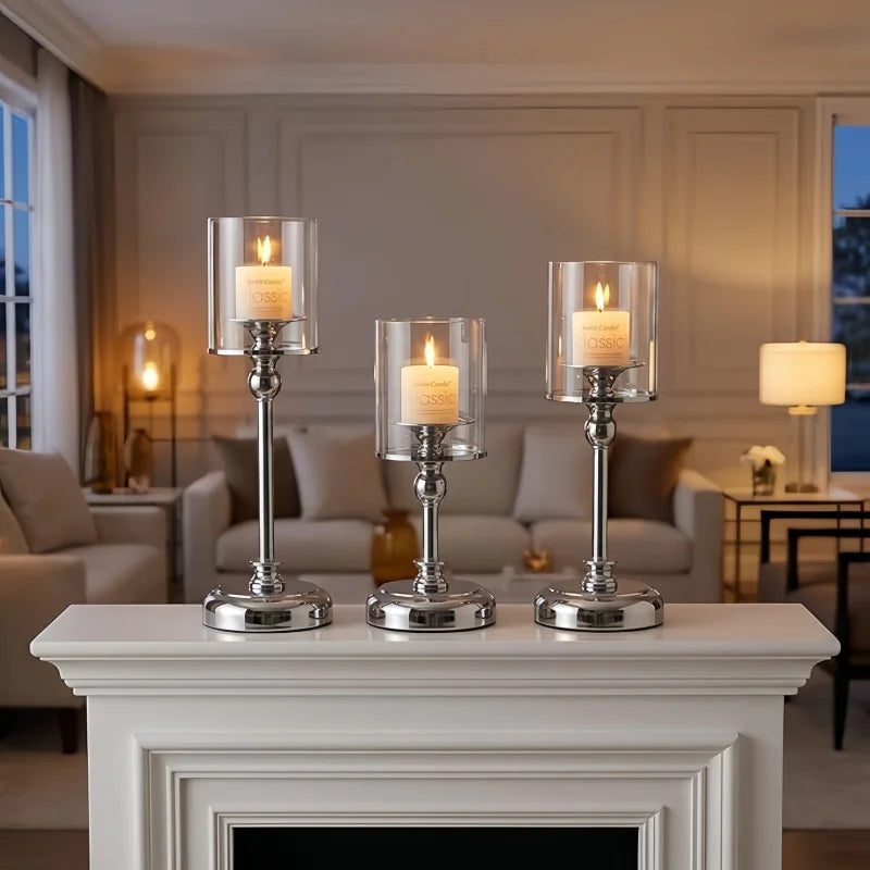 Three silver metal pillar candle holders with lit candles displayed on a white mantelpiece.