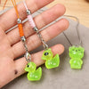 A hand holds several glow-in-the-dark resin charms shaped like an alien cat and a duck, attached to silver chains.