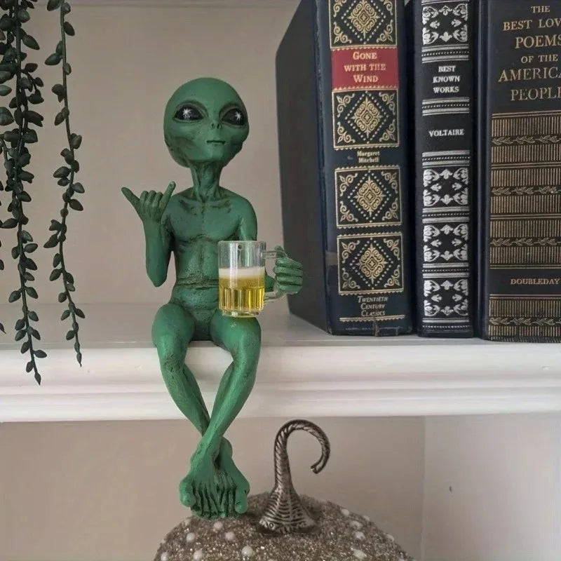 Resin green alien statue holding a glass of beer on a shelf next to books