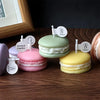 A display of colorful macaron-shaped soy wax candles in pink, green, and yellow on a wooden surface.