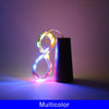 A glowing multicolored wire light shaped like a loop rests next to a black bottle.